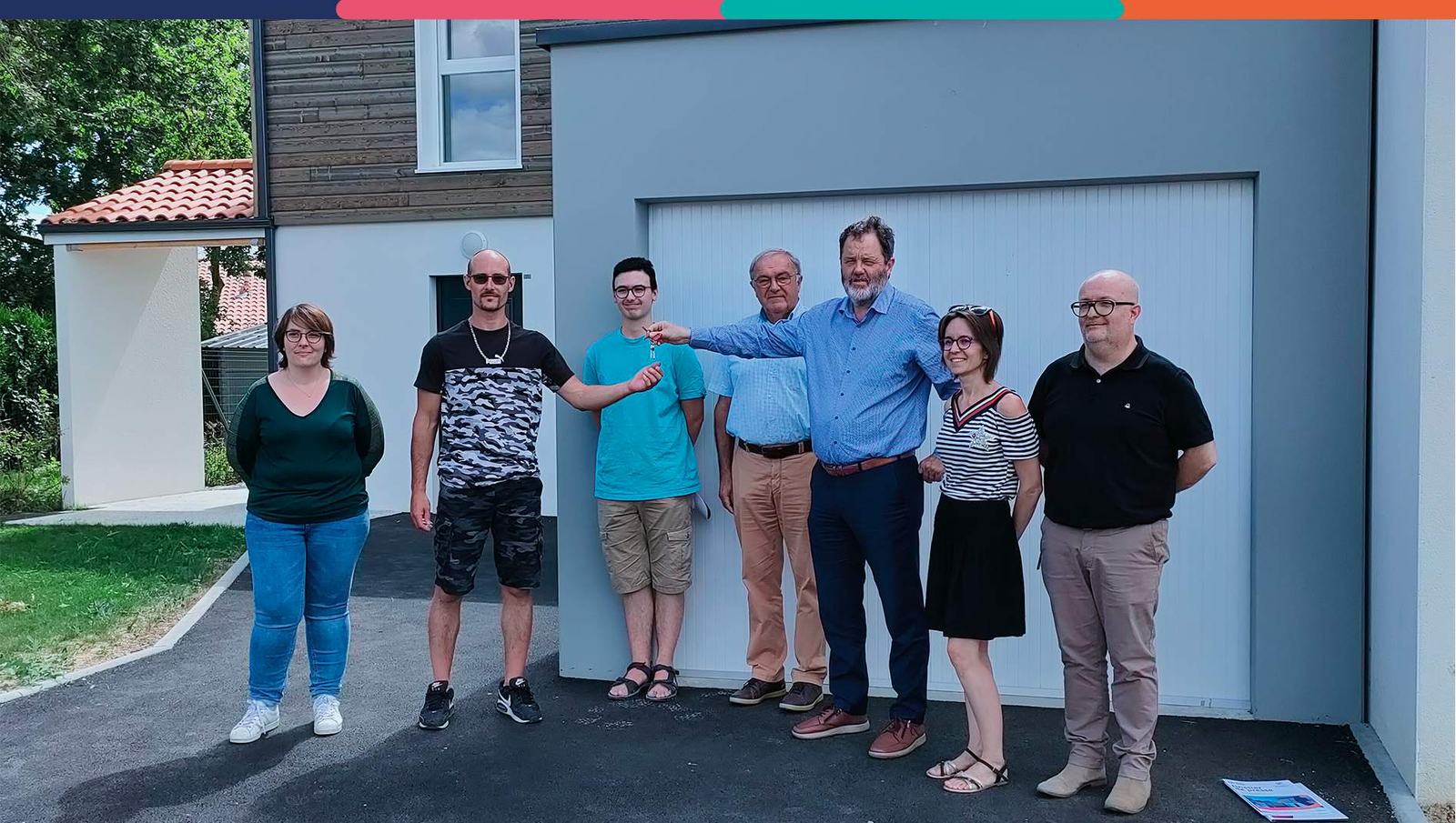 Il s'agit d'une photo de groupe sur laquelle il y a une remise de clefs devant une maison.